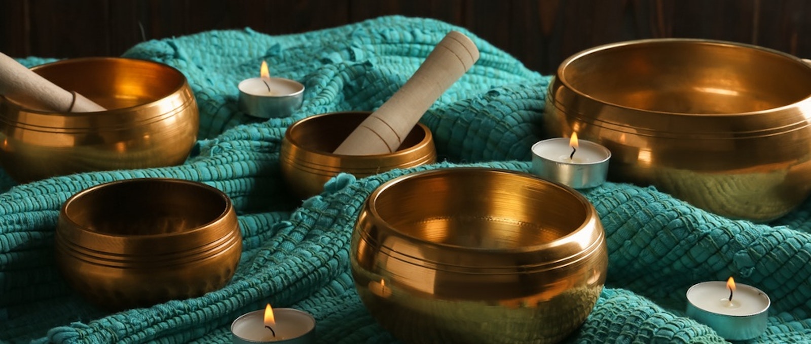 Tibetan singing bowls with mallets, burning candles and turquoise fabric on wooden table