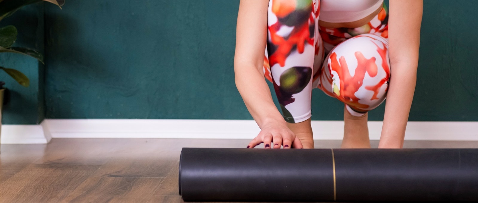 Woman unrolling mat on wooden floor near decorative pot-plant