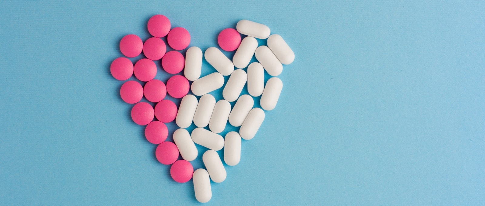 Pink and white pills in heart shape on blue background