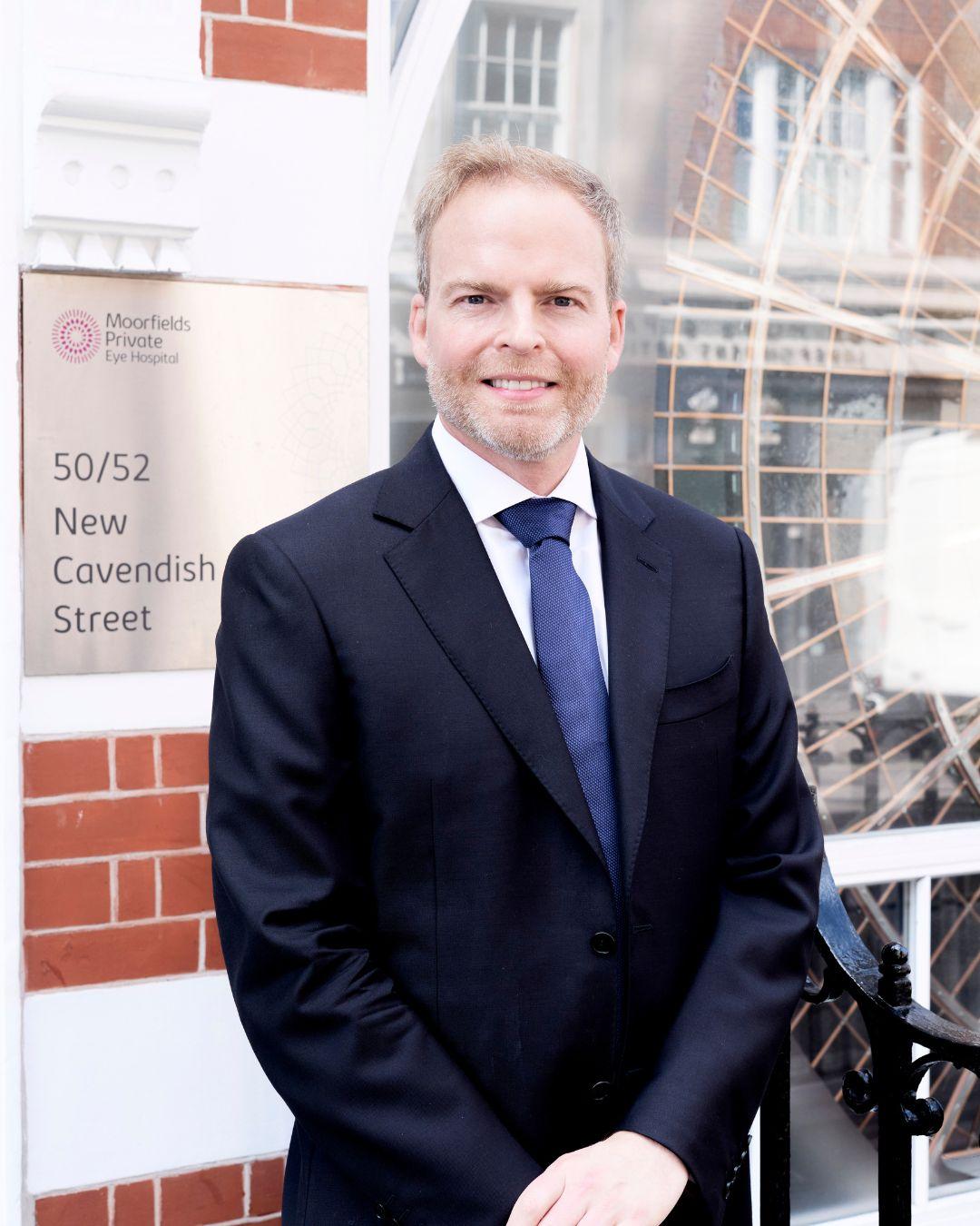Mr Alex Day, Consultant Ophthalmologist, London, UK - short-haired, Caucasian man in white shirt, blue suit and tie standing outside Moorfields Private Eye Hospital on 50/52 Cavendish Street, London