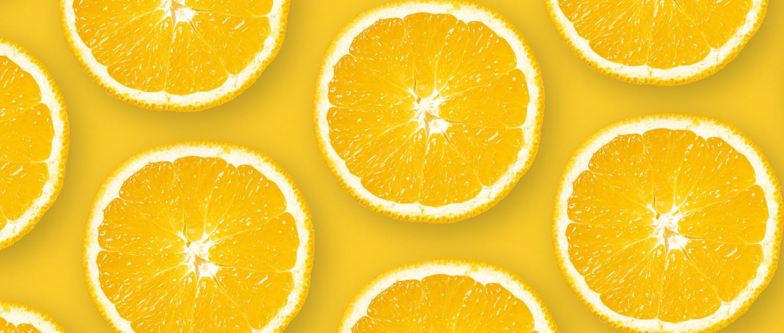 Top view of a pattern made of sliced oranges against an orange background.