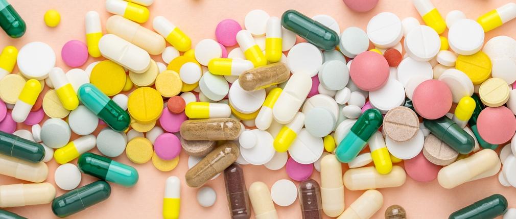 Many different pills and vitamins on pink background.