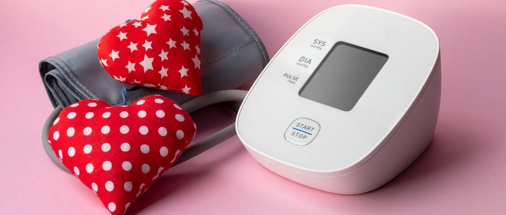 Automatic blood pressure monitor and two soft red hearts on pink background. Medical electronic tonometer
