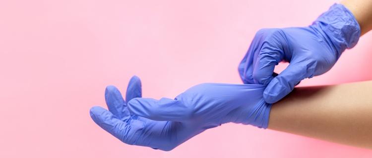 Blue surgical gloved hands against a pink background.
