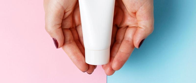 Female hands holding white lotion bottle against split blue and pink background.