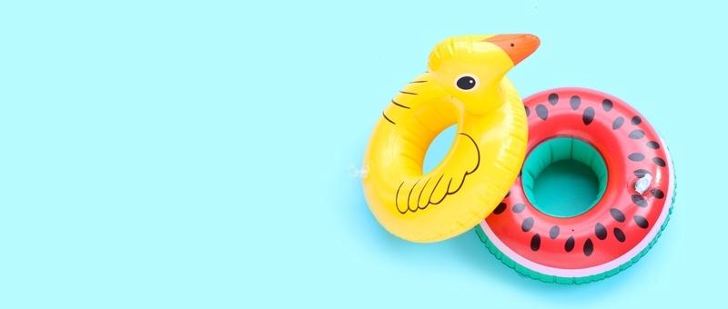 Inflatable yellow duck and watermelon pool toys against pale blue background.