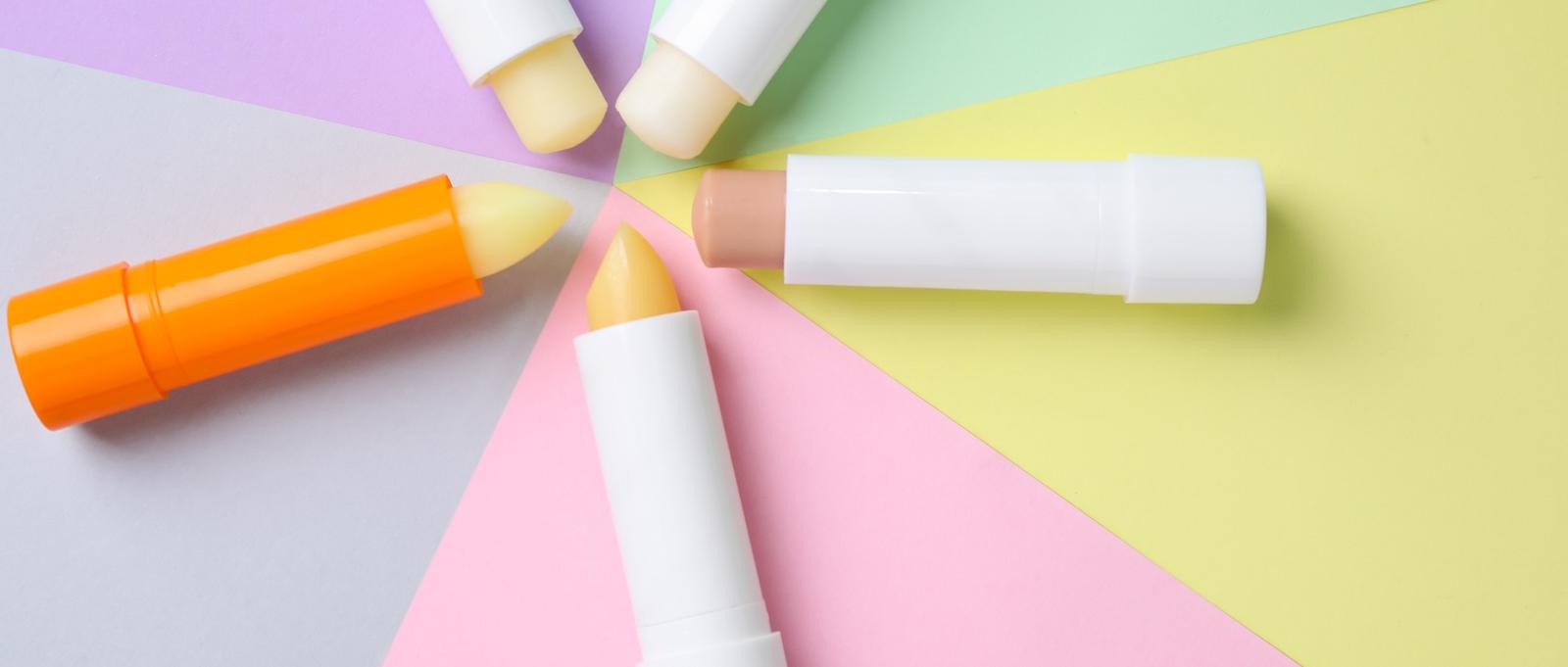 Colourful lip balms arranged in a circle on pastel background sections of purple, pink, yellow and green.