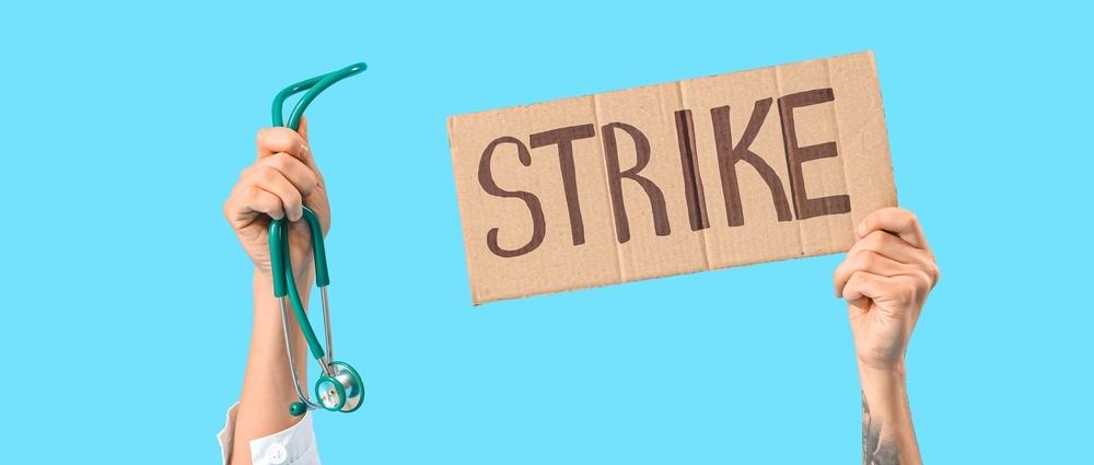 Protesting male doctor holding placard with word STRIKE and stethoscope on blue background