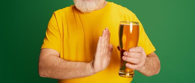 Portrait of senior man in yellow T-shirt posing with beer isolated on green background. Rejecting alcohol drinks.