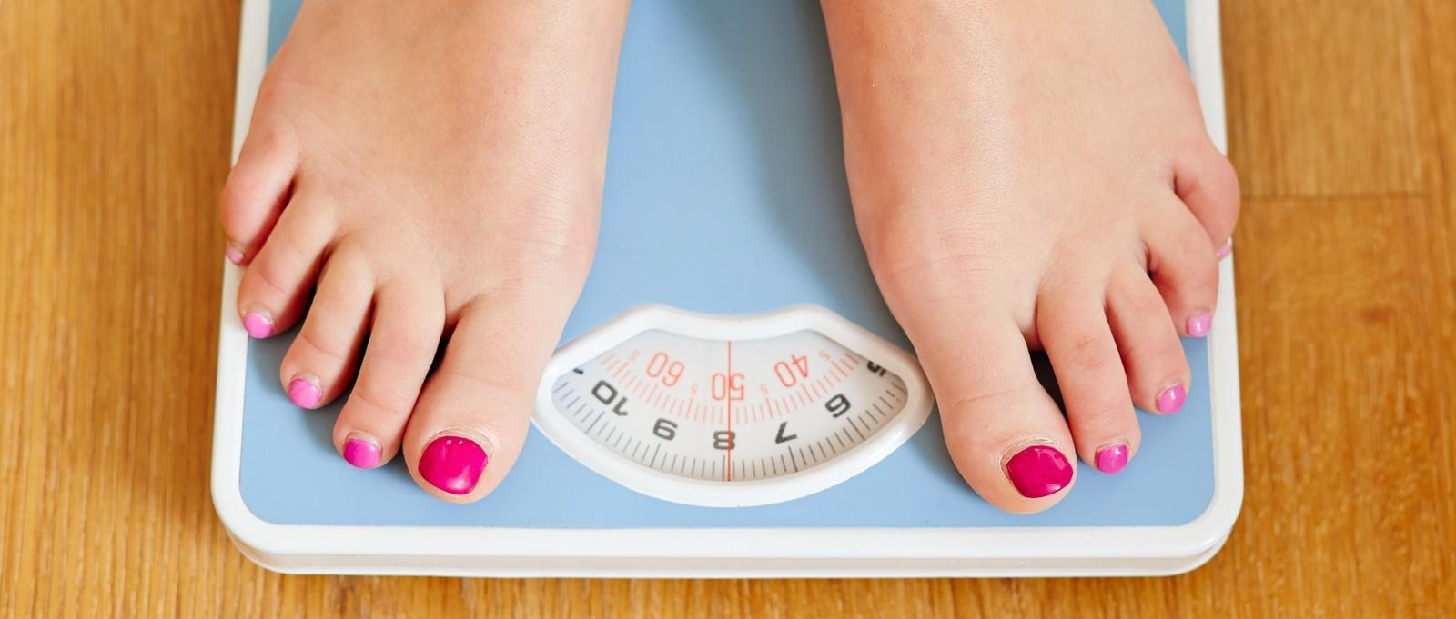 Female bare feet with weight scale on wooden floor