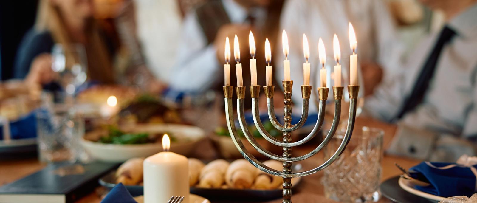 Lit menorah with Jewish extended family in the background on Hanukkah.