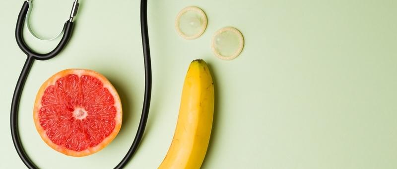 Stethoscope with grapefruit slice and banana against green background.