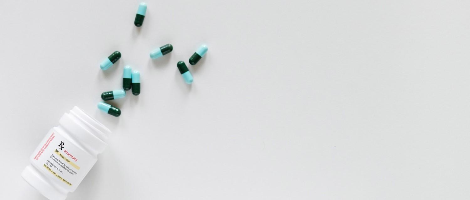 Green and light blue aspirin capsules scattered from a white prescription bottle on a light grey background.