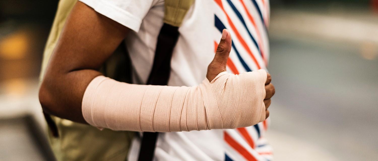Person wearing a white shirt with red and blue stripes showing a hand and forearm wrapped in beige bandage.