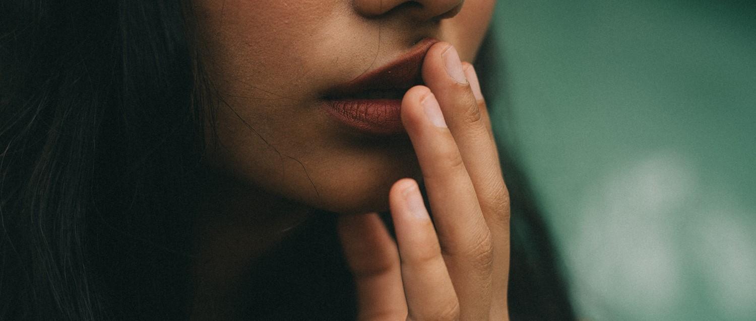 Close-up of a person with red lips touching their face thoughtfully against a soft green background.