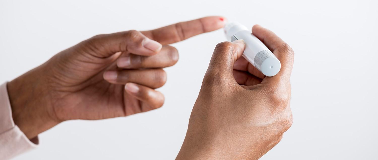 Hands holding a white medical device, possibly a blood glucose meter or insulin pen, against a light background.