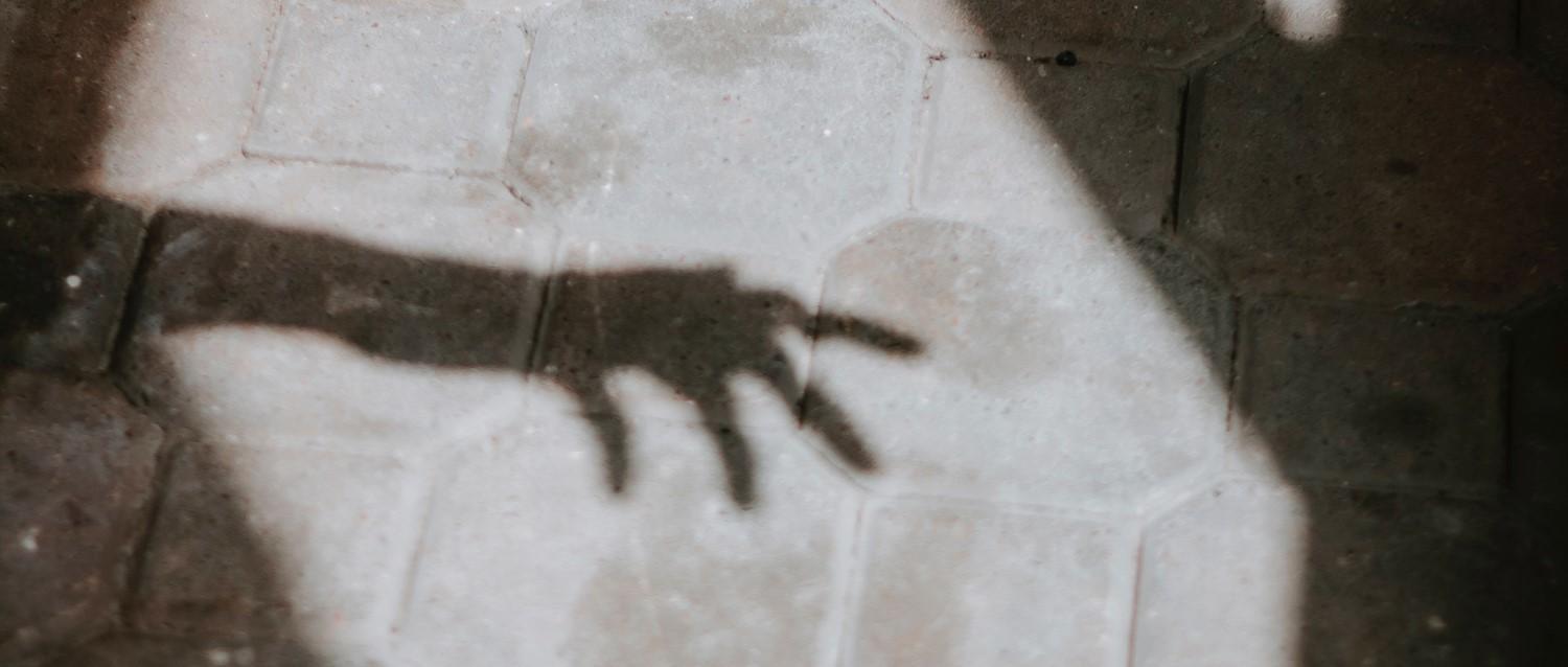 Shadow of a hand cast on a tiled floor, creating a dramatic silhouette against the light-coloured surface.