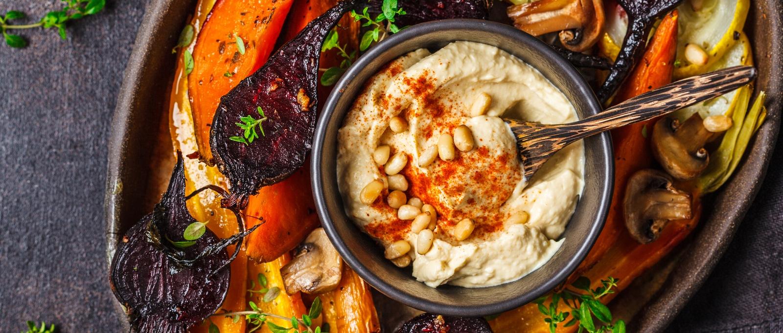 Baked carrots, beets, zucchini and yam with hummus in a dark dish.