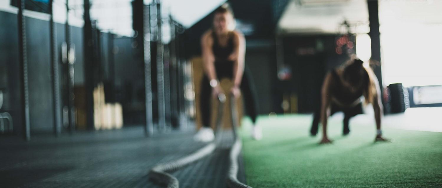 Blurred figures exercising in a modern gym with green flooring, focusing on strength training in a dark setting.